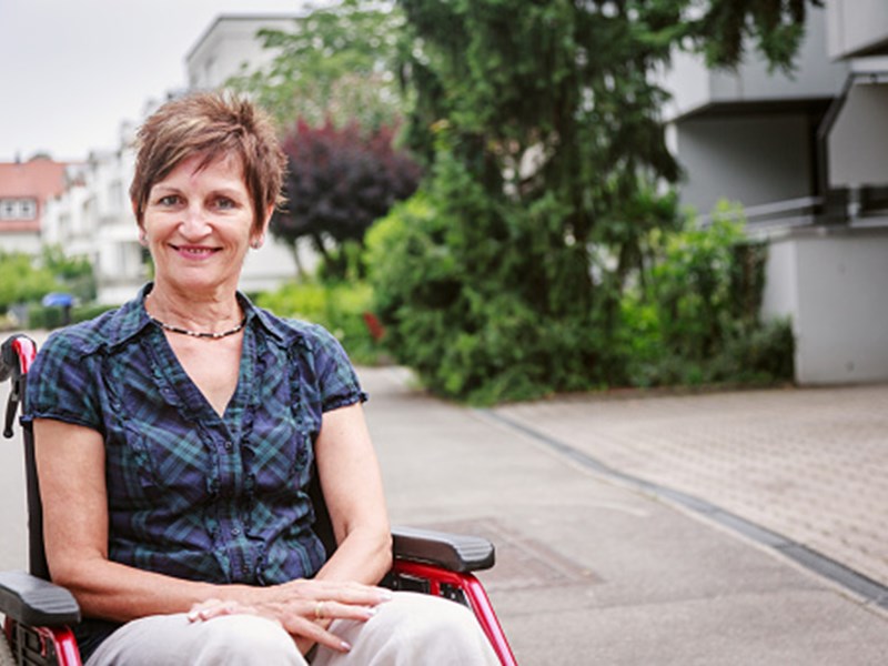 smiling woman in wheelchair in front of apartment building