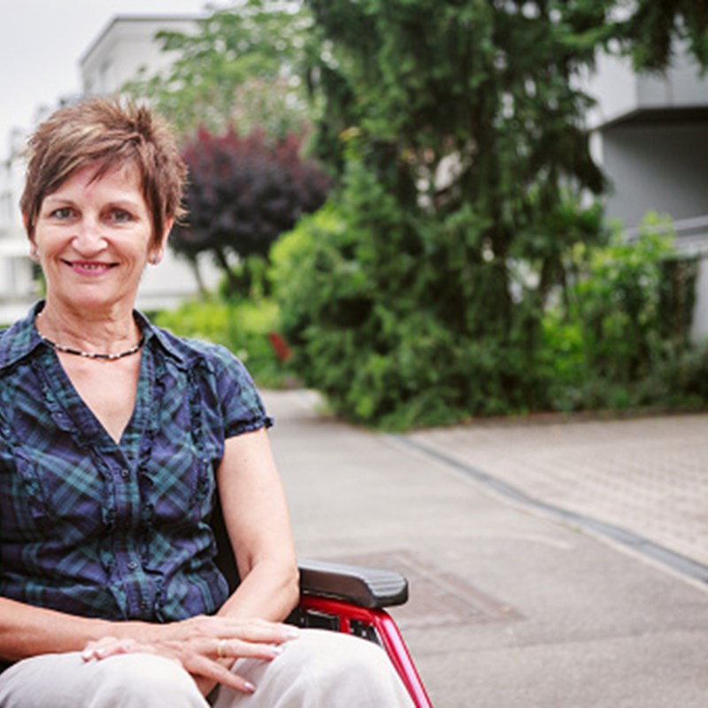 smiling woman in wheelchair in front of apartment building