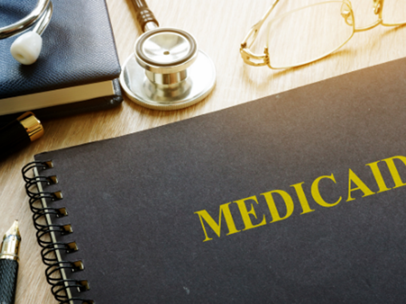 spiral notepad with "MEDICAID" on cover, pen and stethoscope nearby