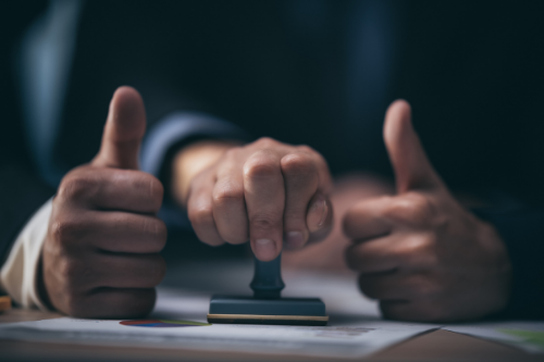 third hand stamping paperwork between two thumbs up