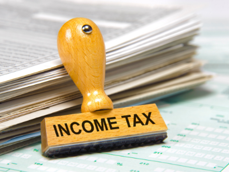 "INCOME TAX" rubber stamp leaning against pile of paperwork